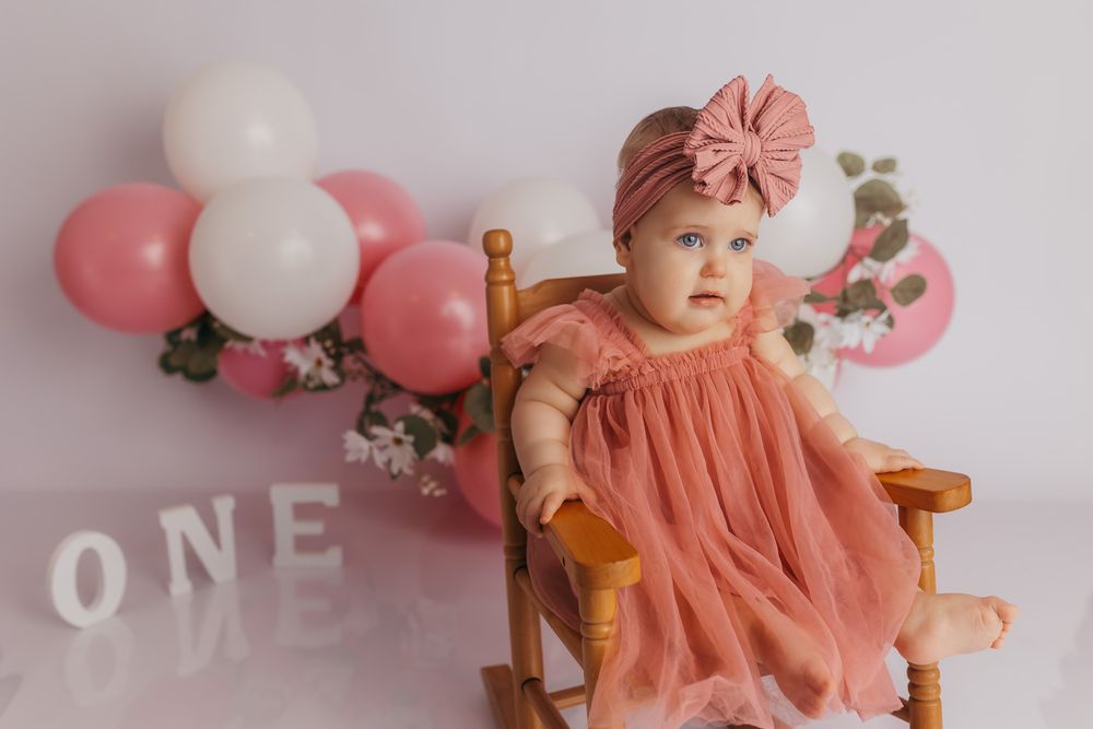 Baby girl rocking a little wooden rocker during her one year cake smash session.