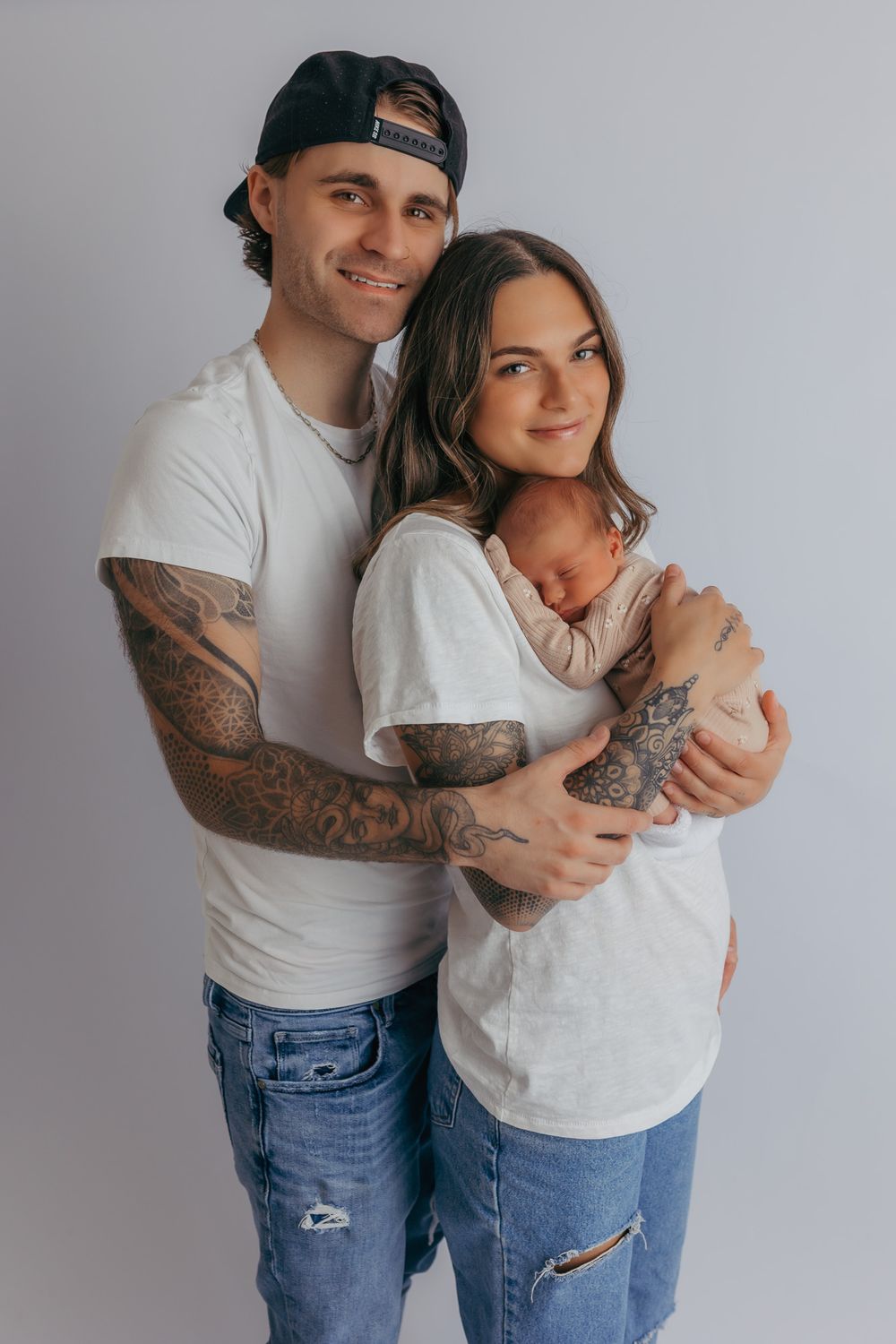 Mom and dad smiling at the camera while holding their newborn during their photography session.