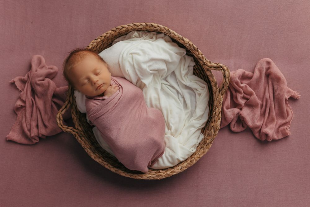 Baby girl wrapped in a pink wrap, and sleeping in a basket.