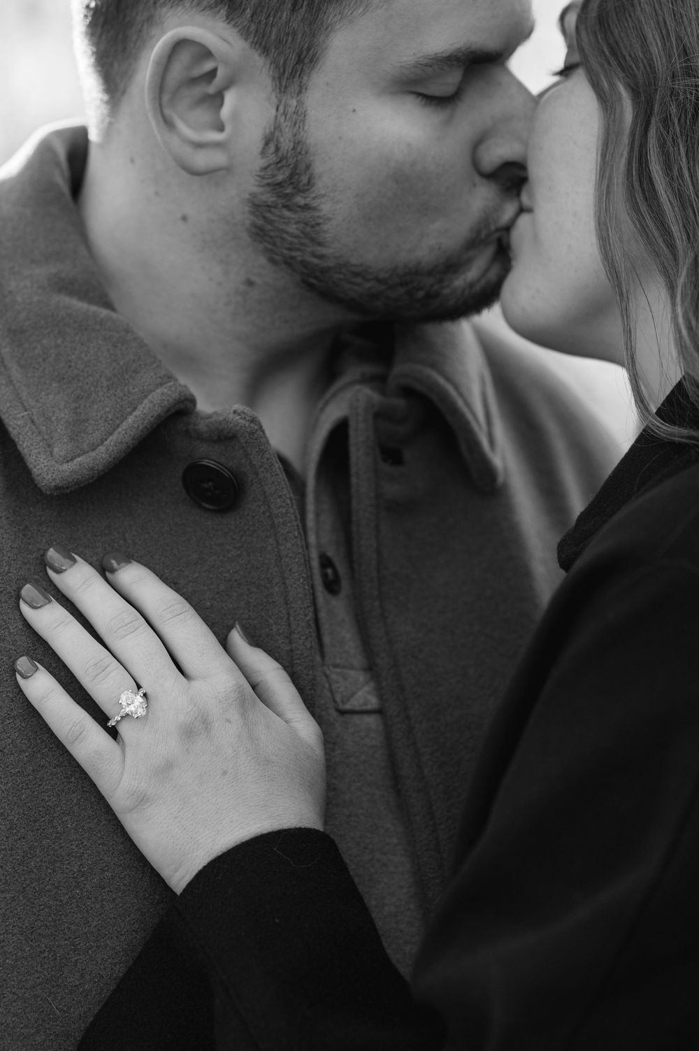 Black and white photo of an engaged couple kissing, showcasing a sparkling engagement ring on the woman's hand.