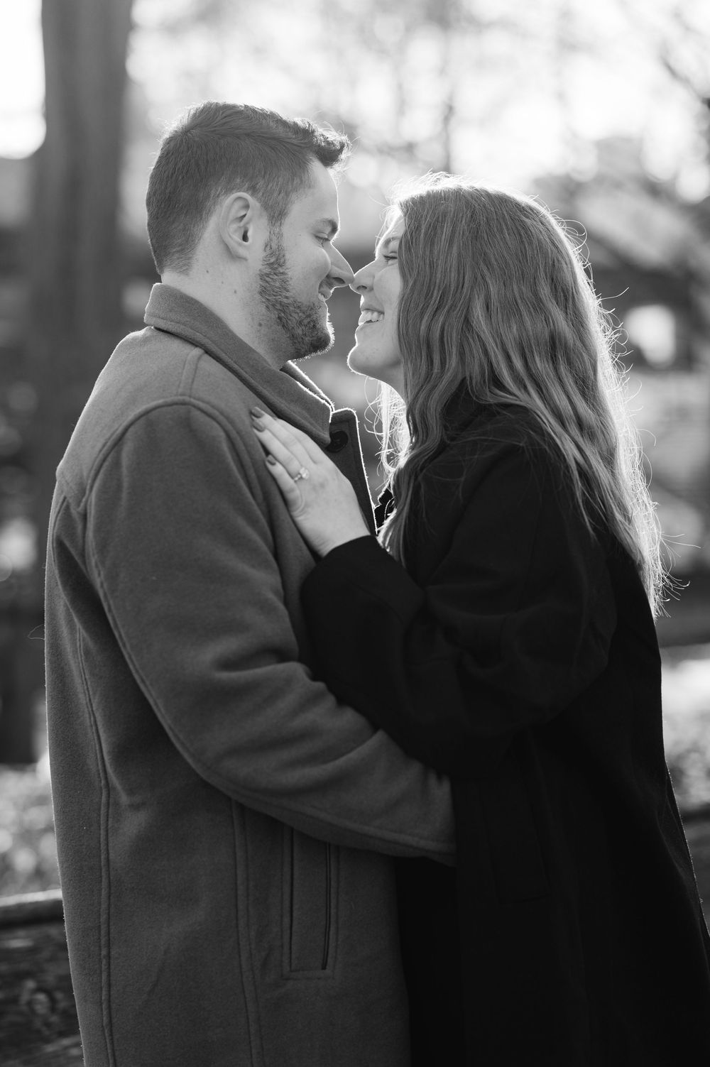 Black and white photo of a couple smiling and embracing outdoors in winter coats.