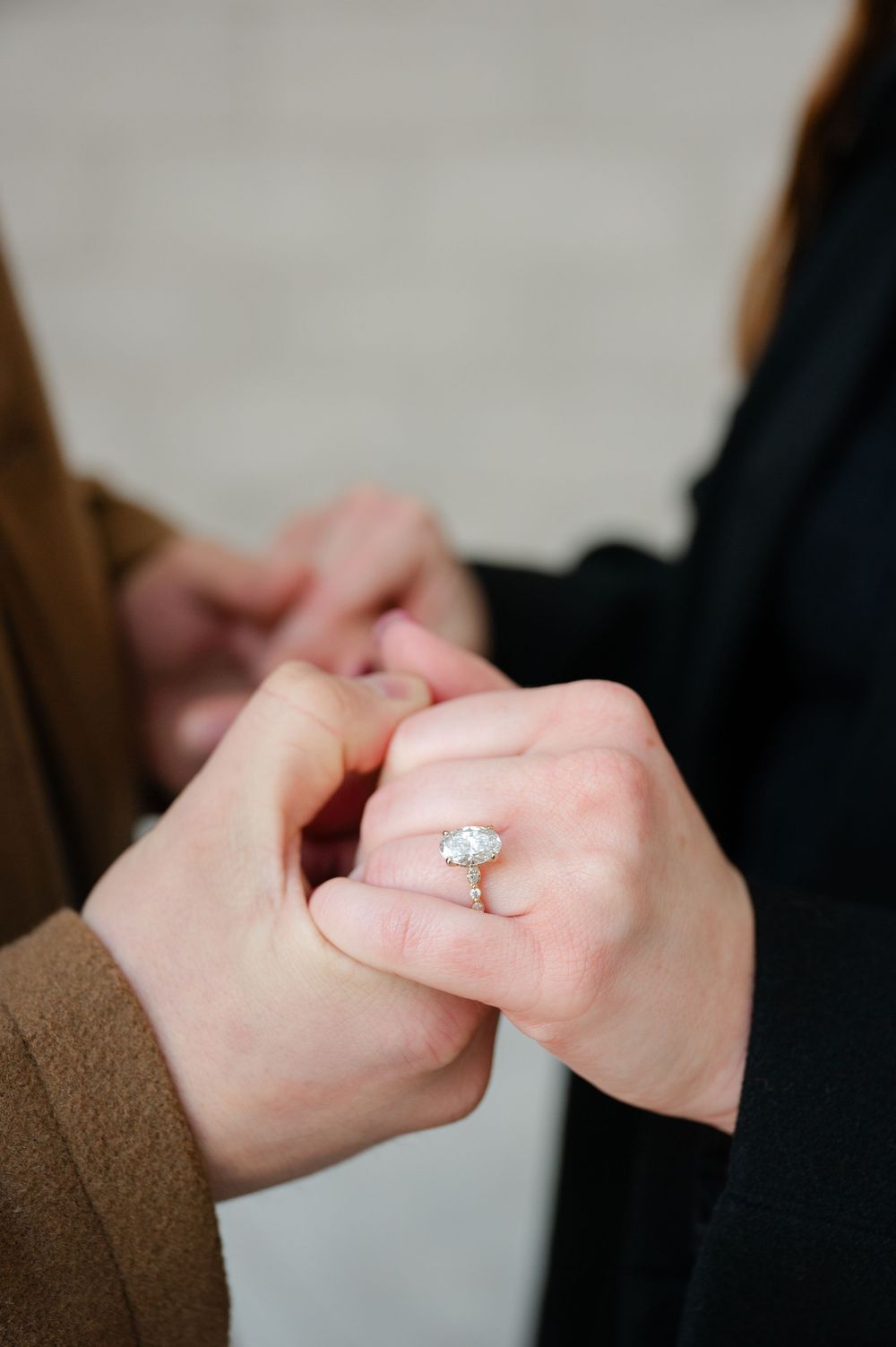 Close-up of oval diamond halo engagement ring on woman's finger being held by partner.