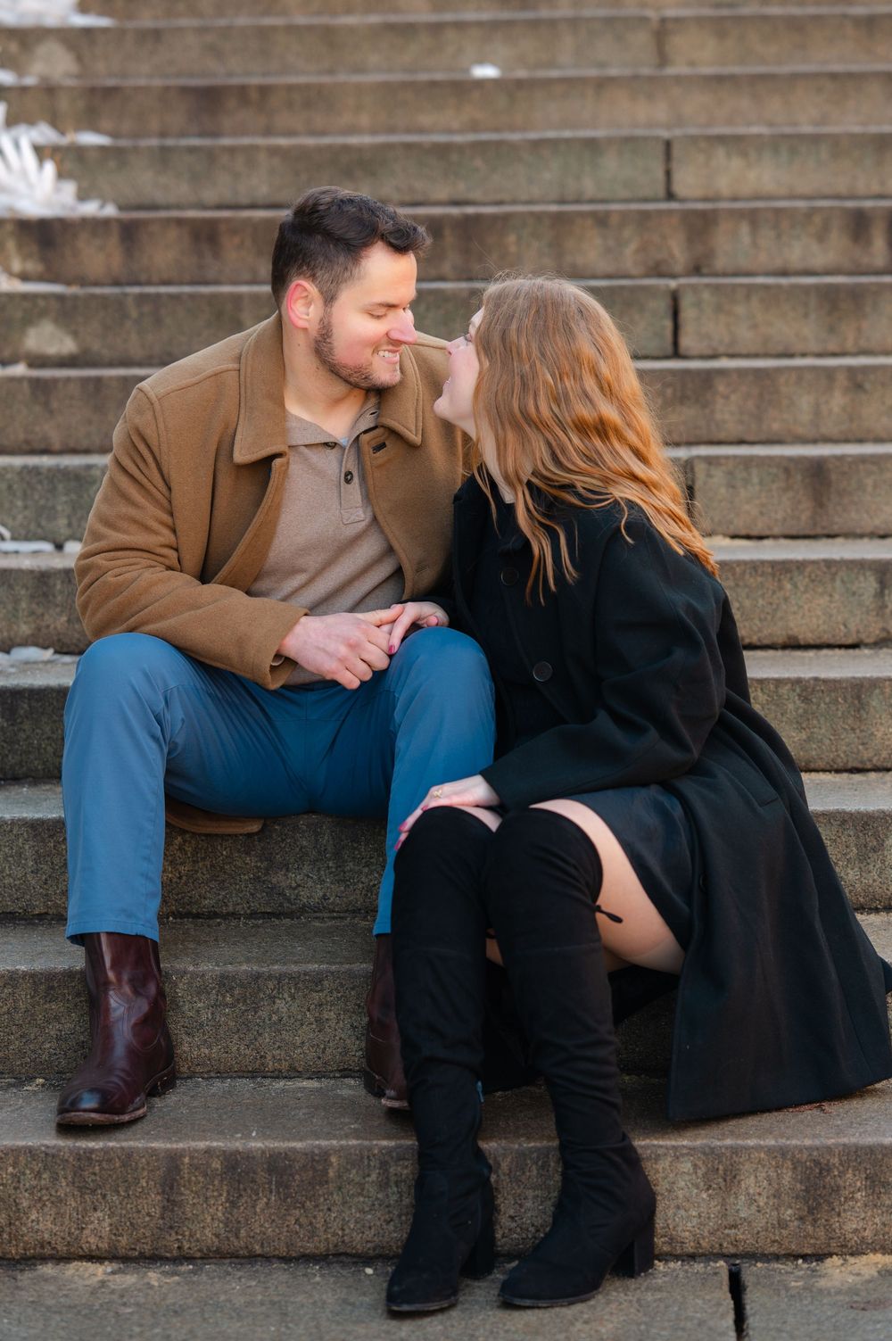 Couple sitting on stone steps sharing a romantic moment, woman wearing knee-high boots.