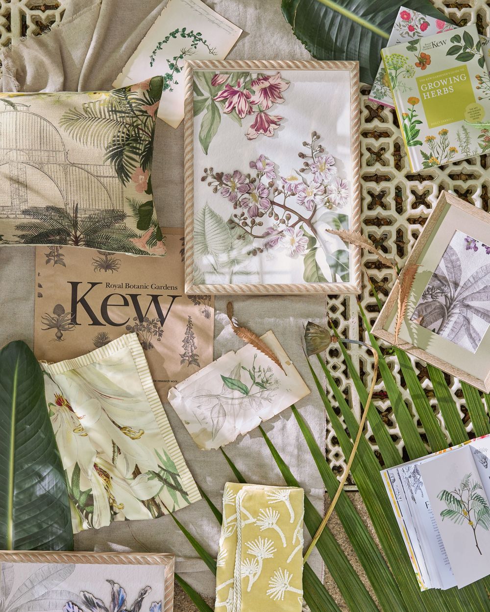 Flat lay of botanical illustrations, fabric swatches, and a Kew Royal Botanic Gardens book surrounded by tropical leaves.