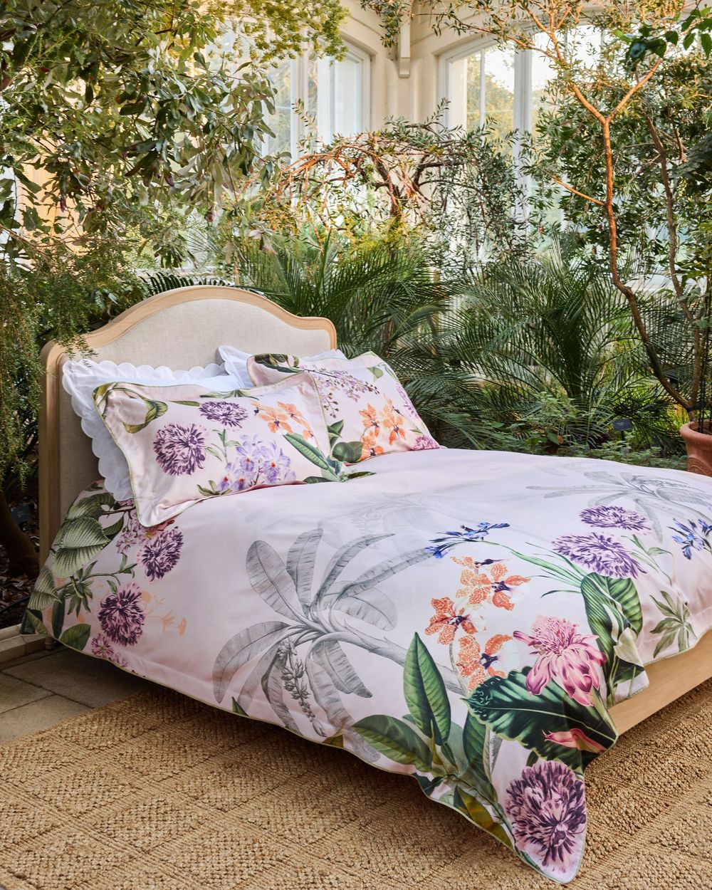 Floral botanical print duvet set on a bed surrounded by lush greenery in a sunlit conservatory setting.