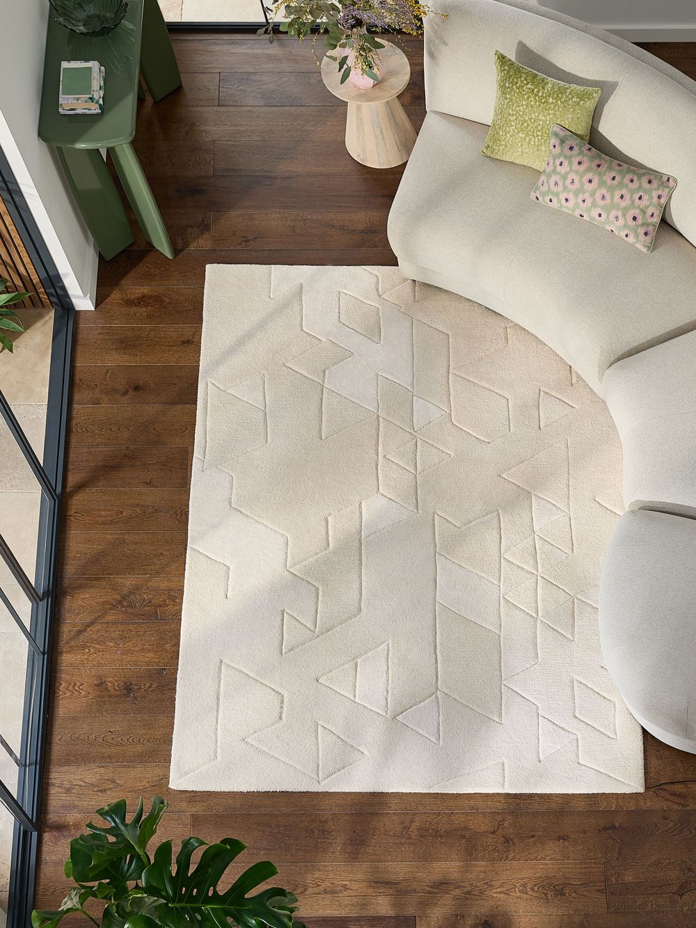 Cream geometric patterned area rug displayed on dark hardwood floor beside a curved white sofa in a modern living room.