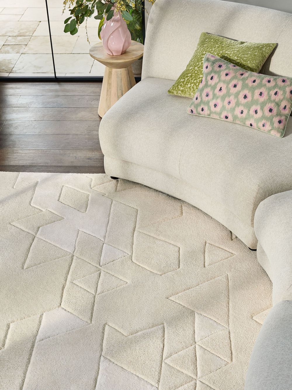 Cream geometric patterned rug beneath a white boucle sofa with green and pink cushions in a modern living room.