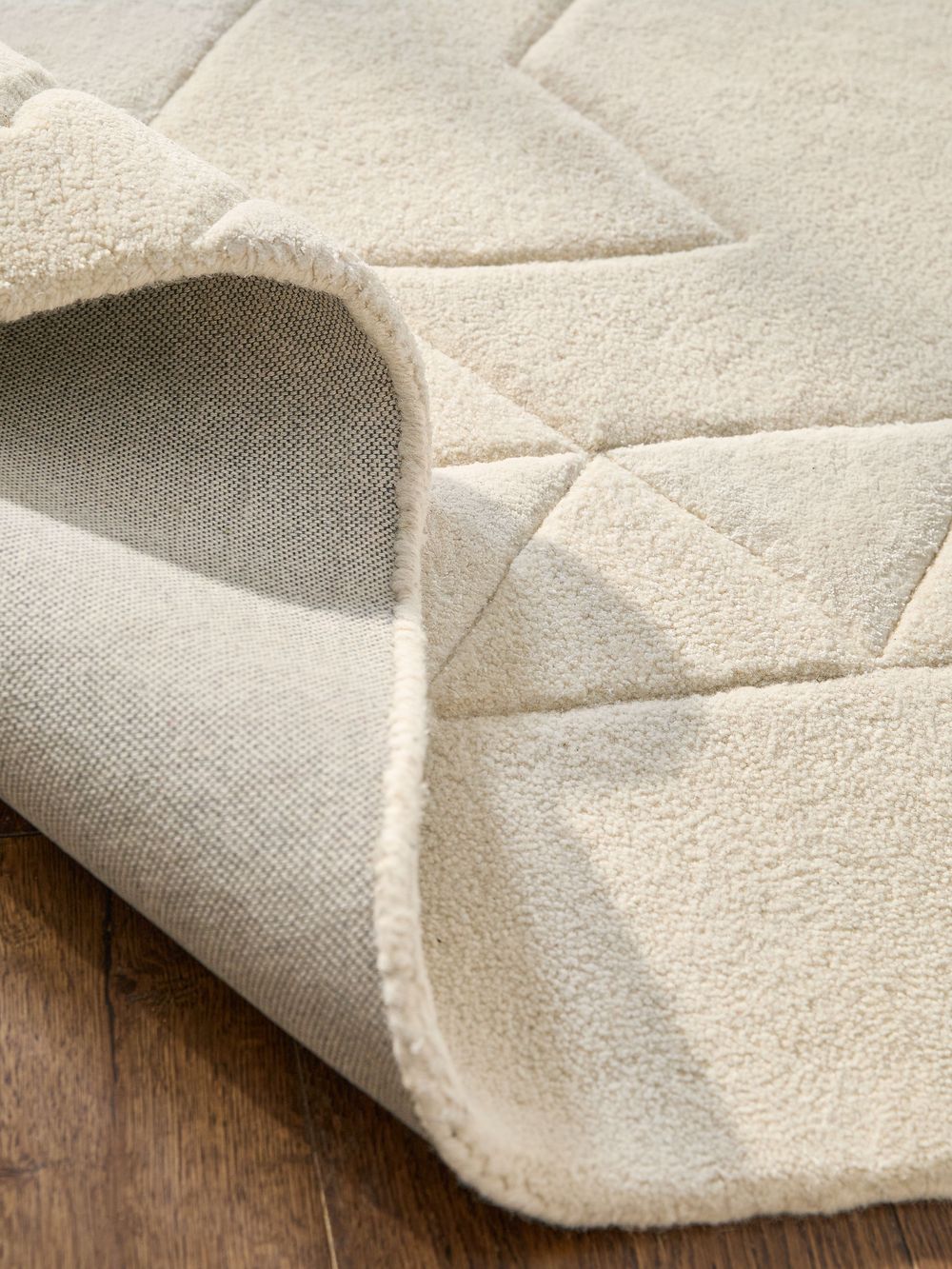 Close-up of a cream quilted rug folded back to reveal its textured backing, resting on a hardwood floor.