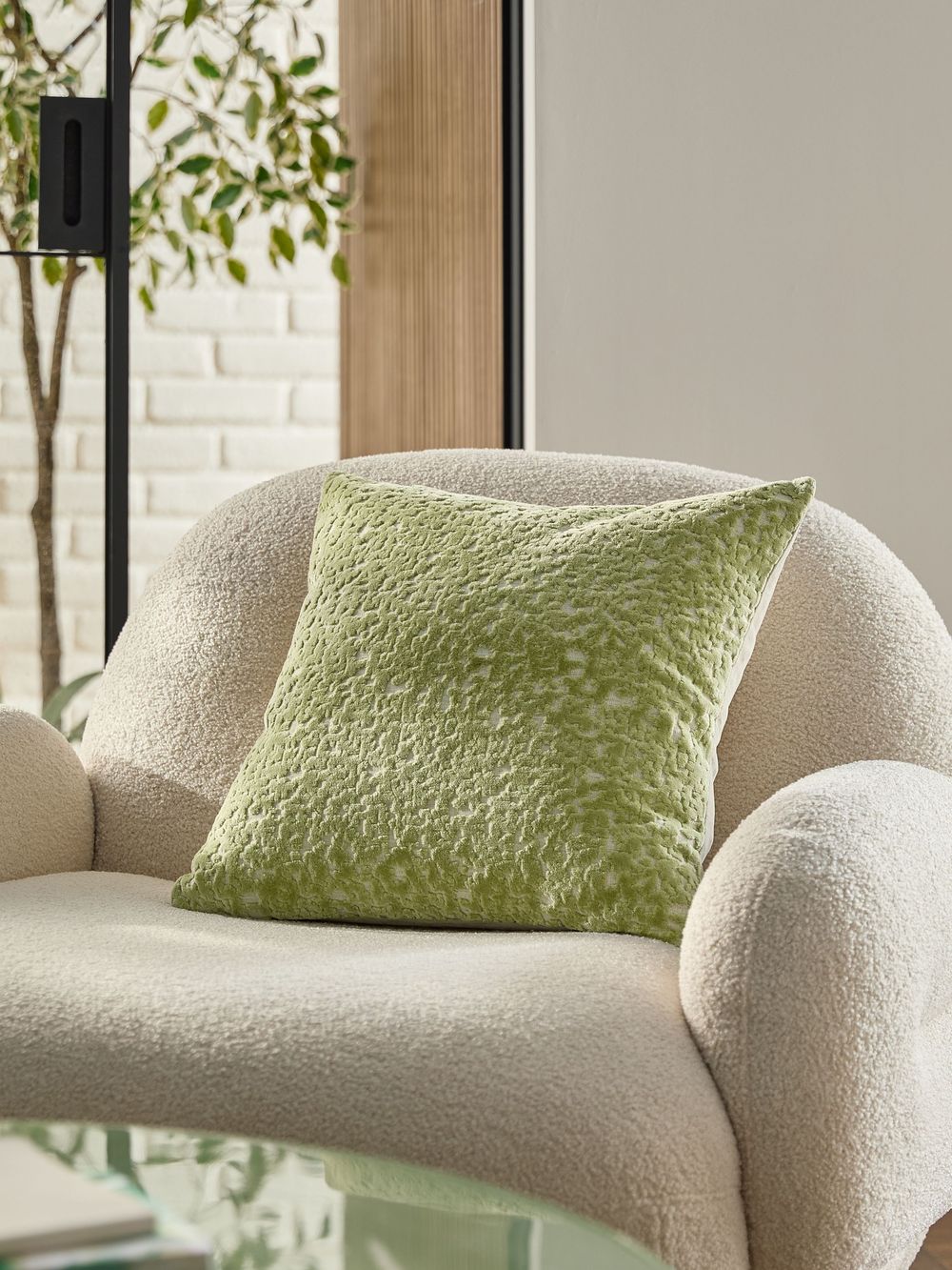 Green textured velvet cushion on a cream boucle armchair in a bright modern living space.
