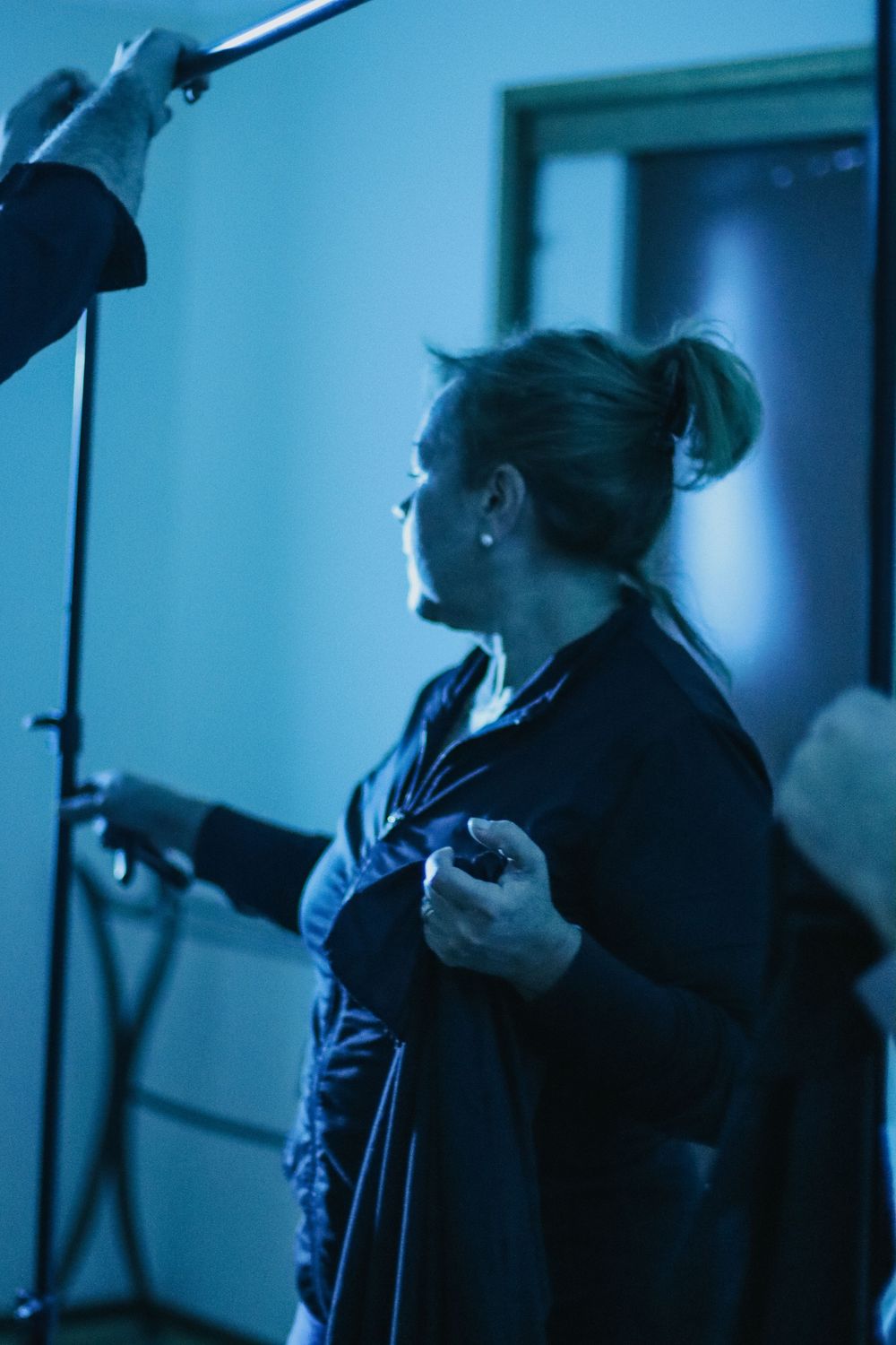 Woman in dark robe holding device under blue studio lighting during a professional photo or film shoot.
