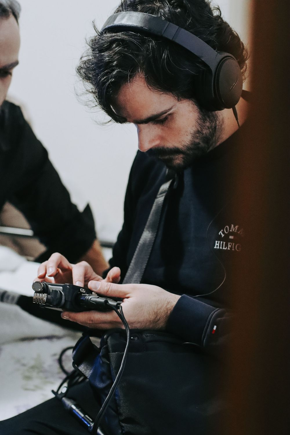 Bearded man wearing headphones and Tommy Hilfiger jacket operating a camera during a film production.