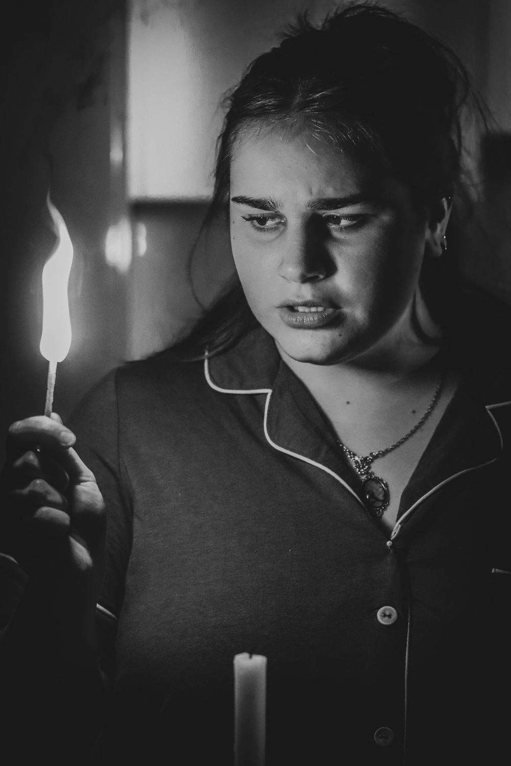 Young woman holding a lit candle in darkness, black and white dramatic portrait photography.