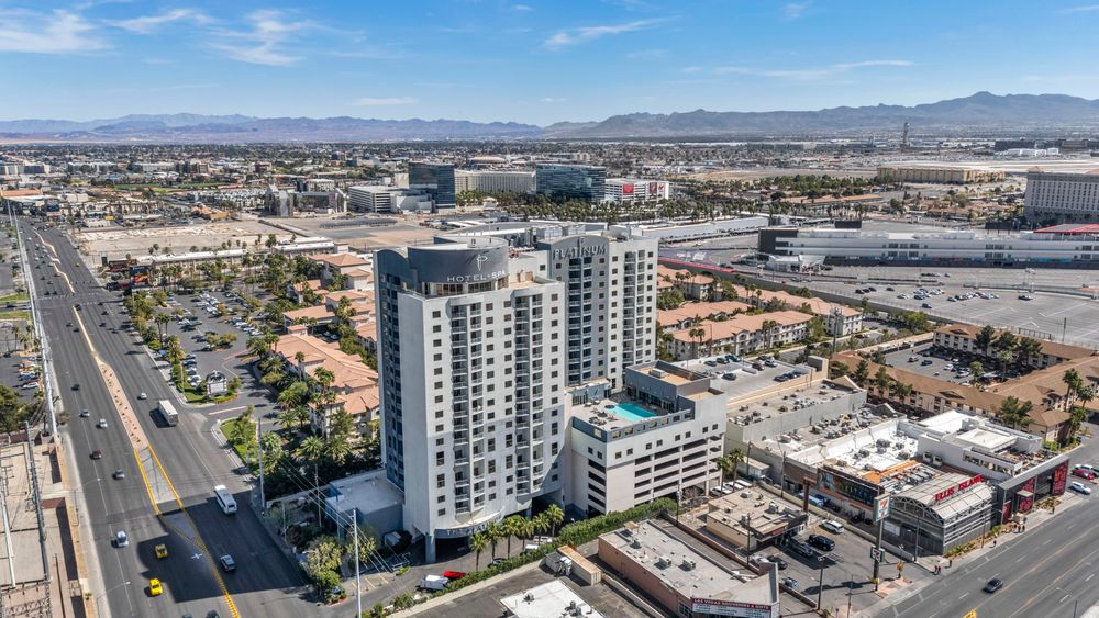 Aerial view of The Platinum Hotel tower rising above Las Vegas streets with mountains in the background.