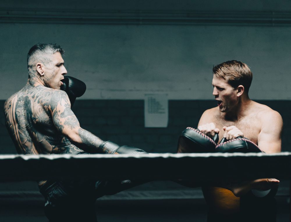 Two tattooed boxers sparring in the ring, mid-action, focused and determined during a boxing match.