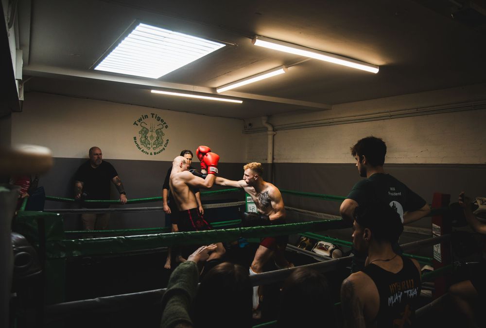 Boxers and trainers gathered around a boxing ring in a gym, captured during an energetic training session with dramatic lighting.