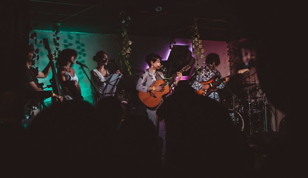 Band performing on stage with colorful lighting in a small intimate music venue.