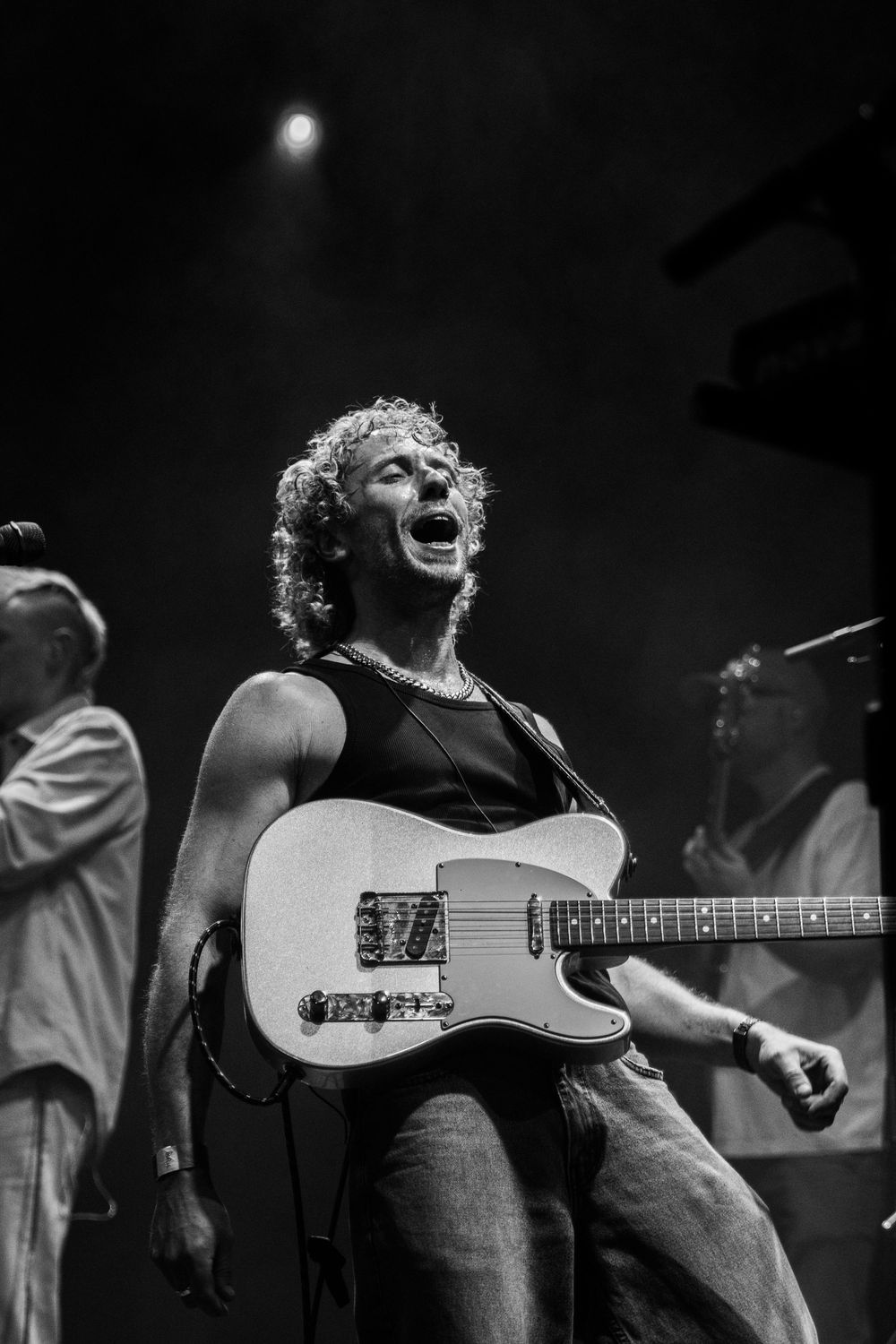 Black and white photo of a curly-haired guitarist singing passionately on stage while playing a Telecaster electric guitar.