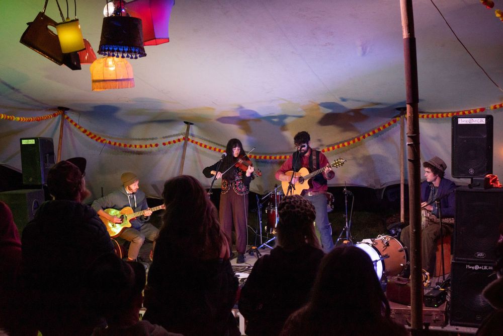 Live band performing on a decorated stage inside a colorful tent venue with an audience watching.