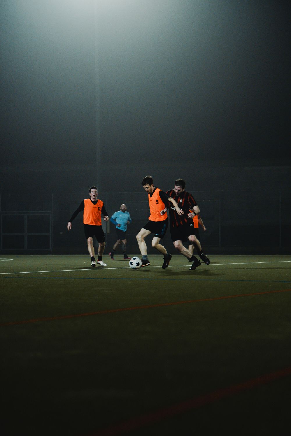 Players compete in a nighttime soccer match under bright floodlights on an outdoor field.