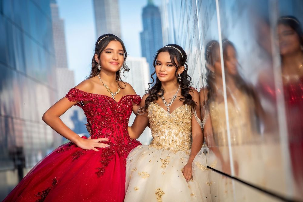 Two young women in elegant quinceañera gowns, one red and one gold, posing together for a formal celebration portrait.