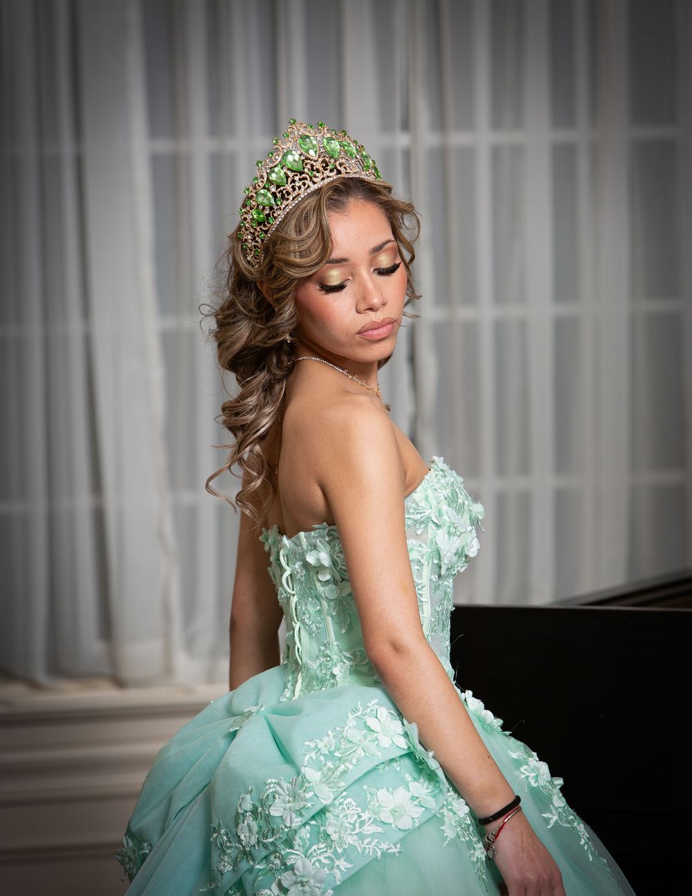 Young woman in mint green ballgown and jeweled tiara poses elegantly for a quinceañera portrait.