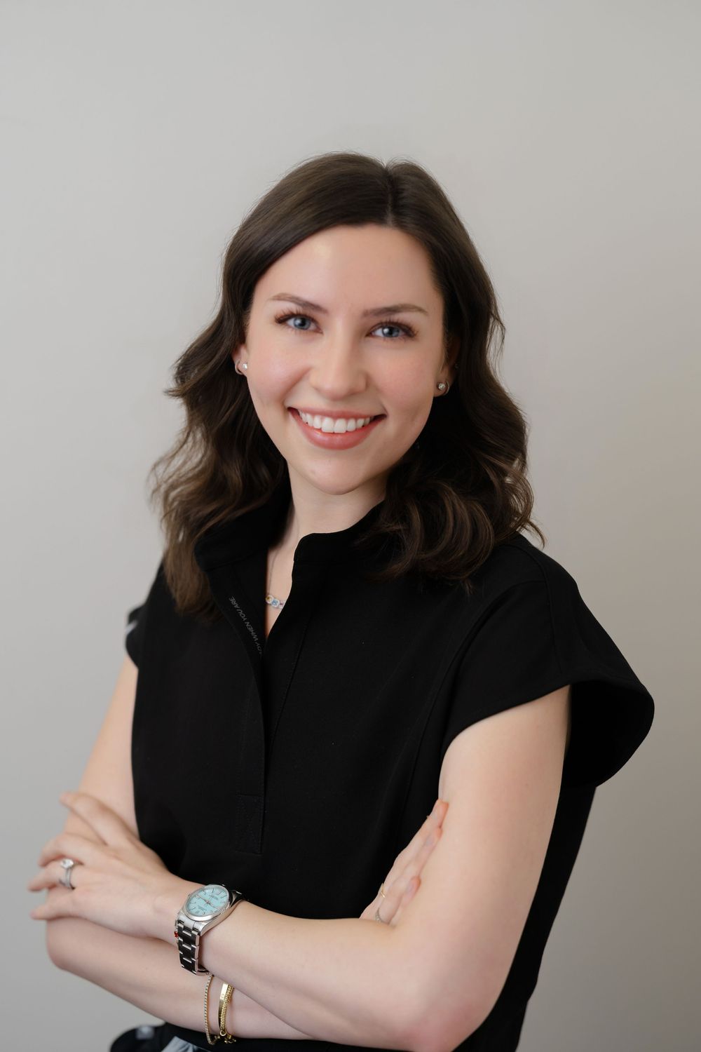Professional woman in black dress smiling with arms crossed against neutral background.