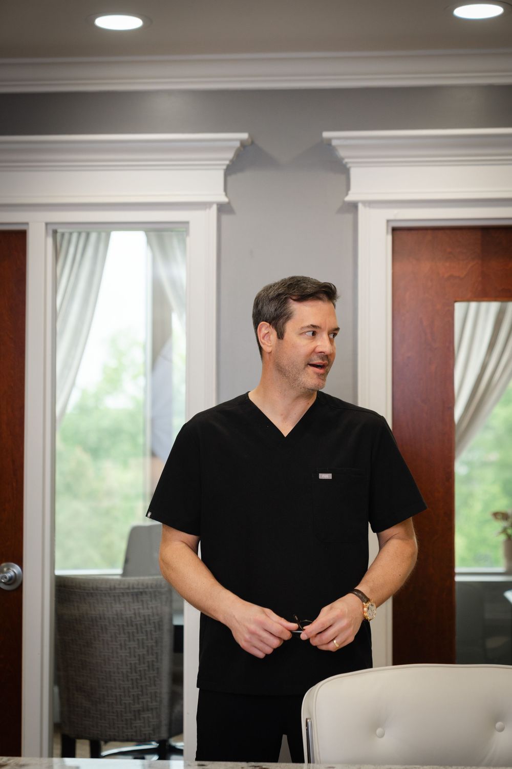 Confident medical professional in black scrubs standing in an elegant clinic consultation room.