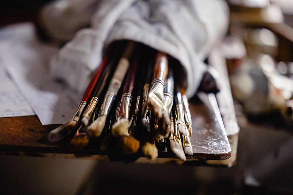 A collection of well-used artist paint brushes bundled together on a wooden surface in a rustic studio setting.