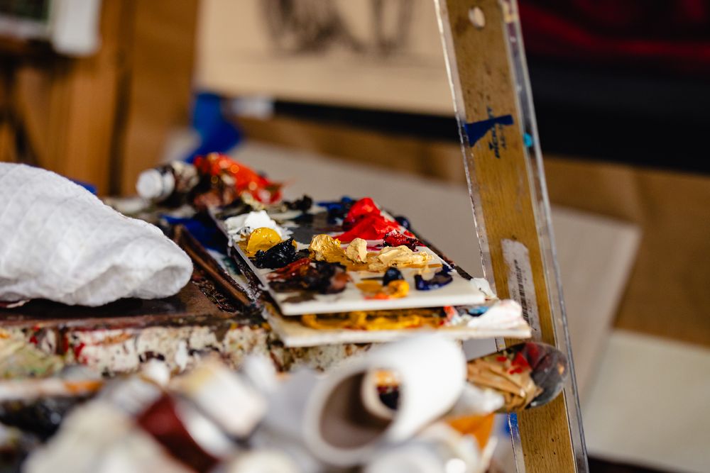 Artist palette with vibrant oil paints beside a wooden easel in a creative studio workspace.