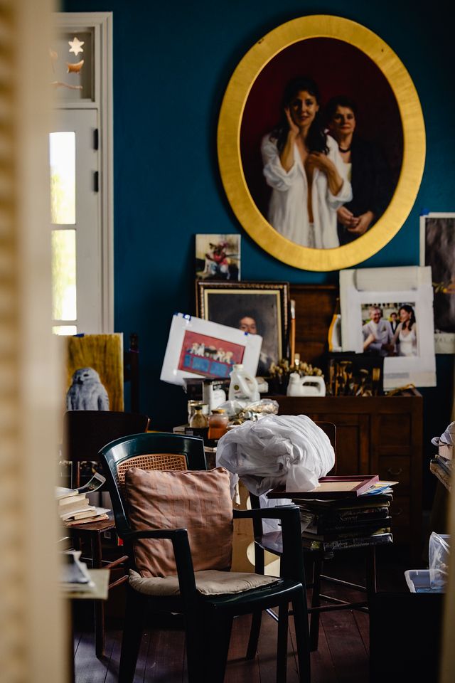 Eclectic room with teal walls, gold oval mirror, vintage photos, and cluttered desk with chairs.