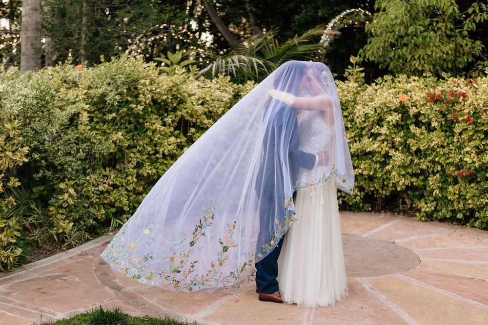 Atmospheric 35mm film photography of a sunset wedding and bride and groom underneath a wedding veil, documenting a chill and candid vibe.