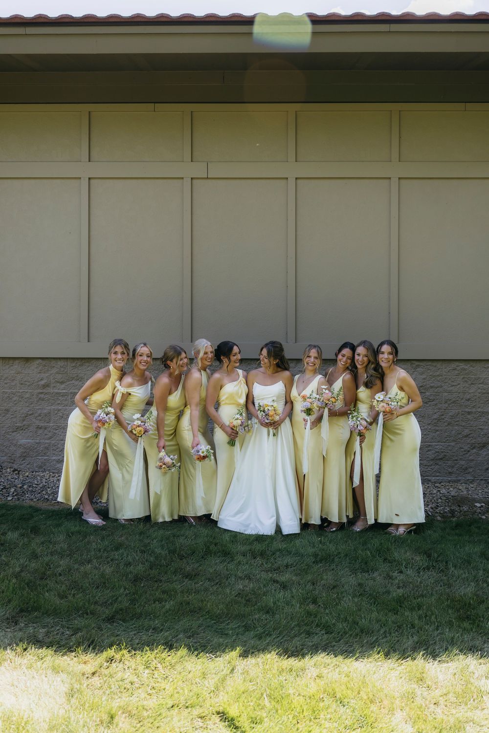 Bride in white gown poses with bridesmaids in yellow dresses holding bouquets outside a building during  Wisconsin wedding day