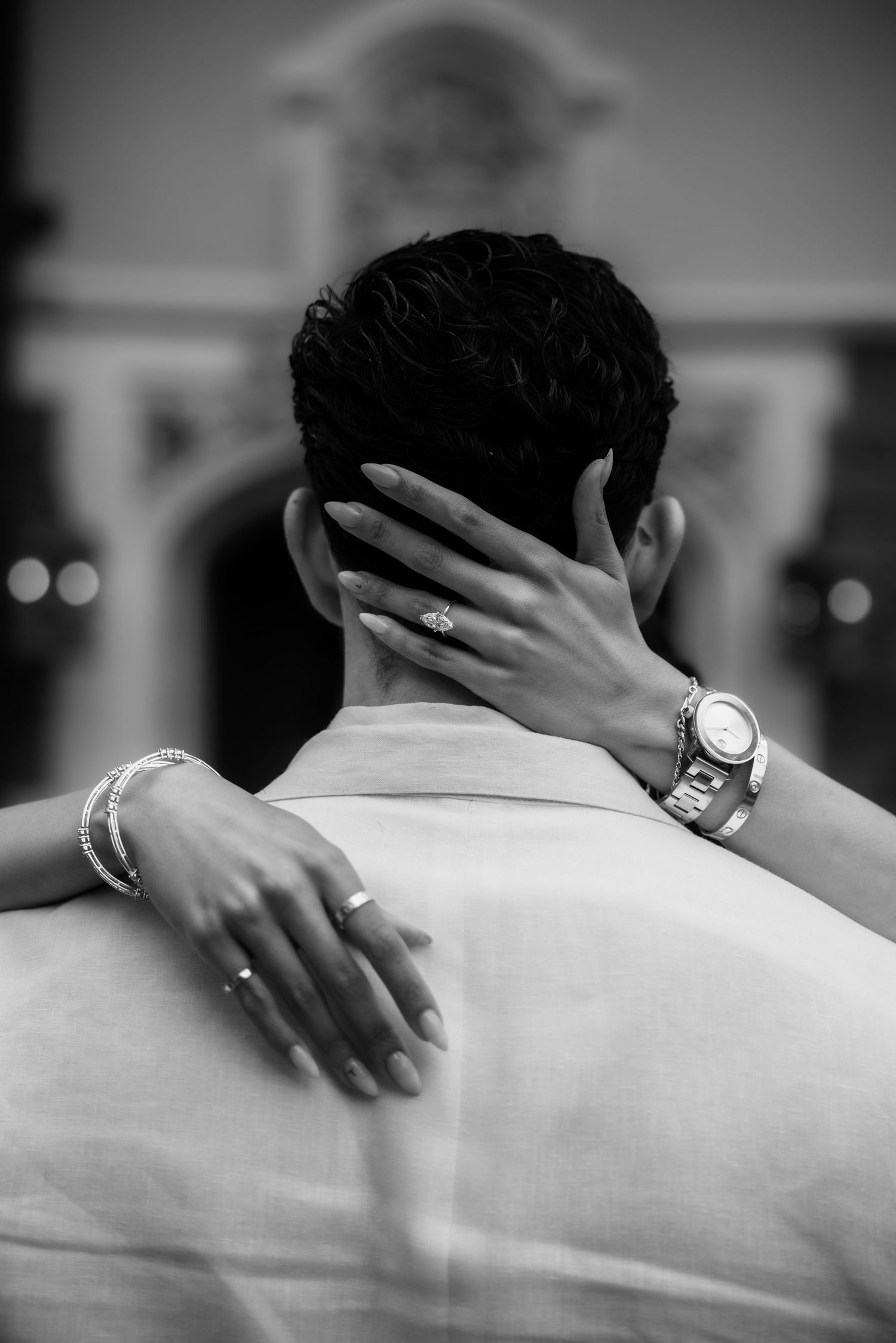 Black and white photo of a bride embracing groom from behind, showing her diamond ring, bracelet, and watch.