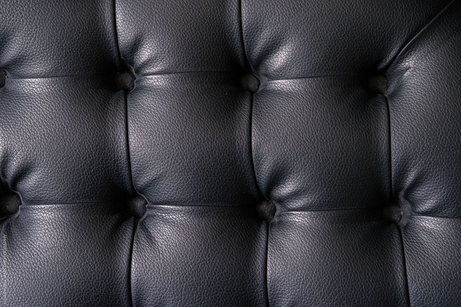 Close-up of tufted black leather upholstery with button details, showcasing a classic Chesterfield sofa texture.