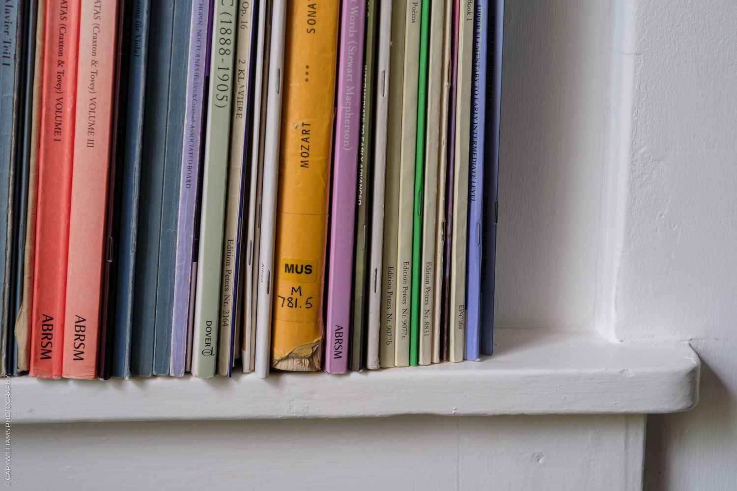 Colorful books and magazines arranged upright on a white wooden shelf, showcasing various spines in pink, yellow, and purple.
