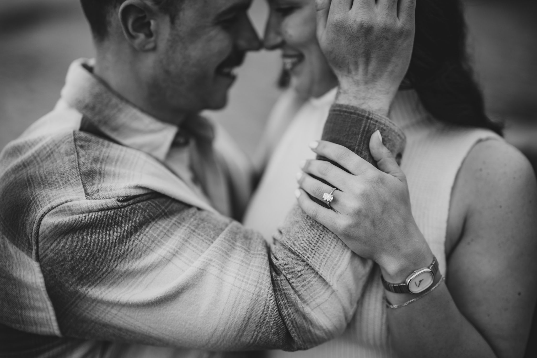 Black and white photo of a couple sharing a romantic moment, woman wearing an engagement ring and watch.