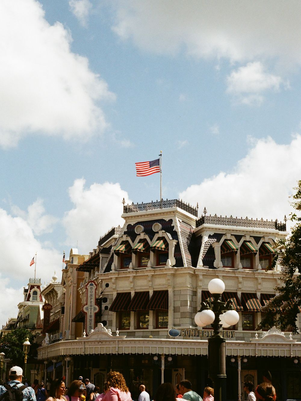American flag atop ornate Main Street USA building at Disney World Magic Kingdom under partly cloudy sky.