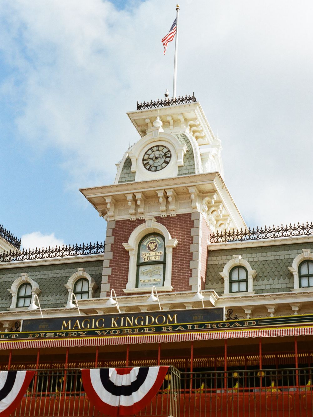 Magic Kingdom entrance building with clock tower, American flag, red brick facade, and patriotic bunting at Walt Disney World.