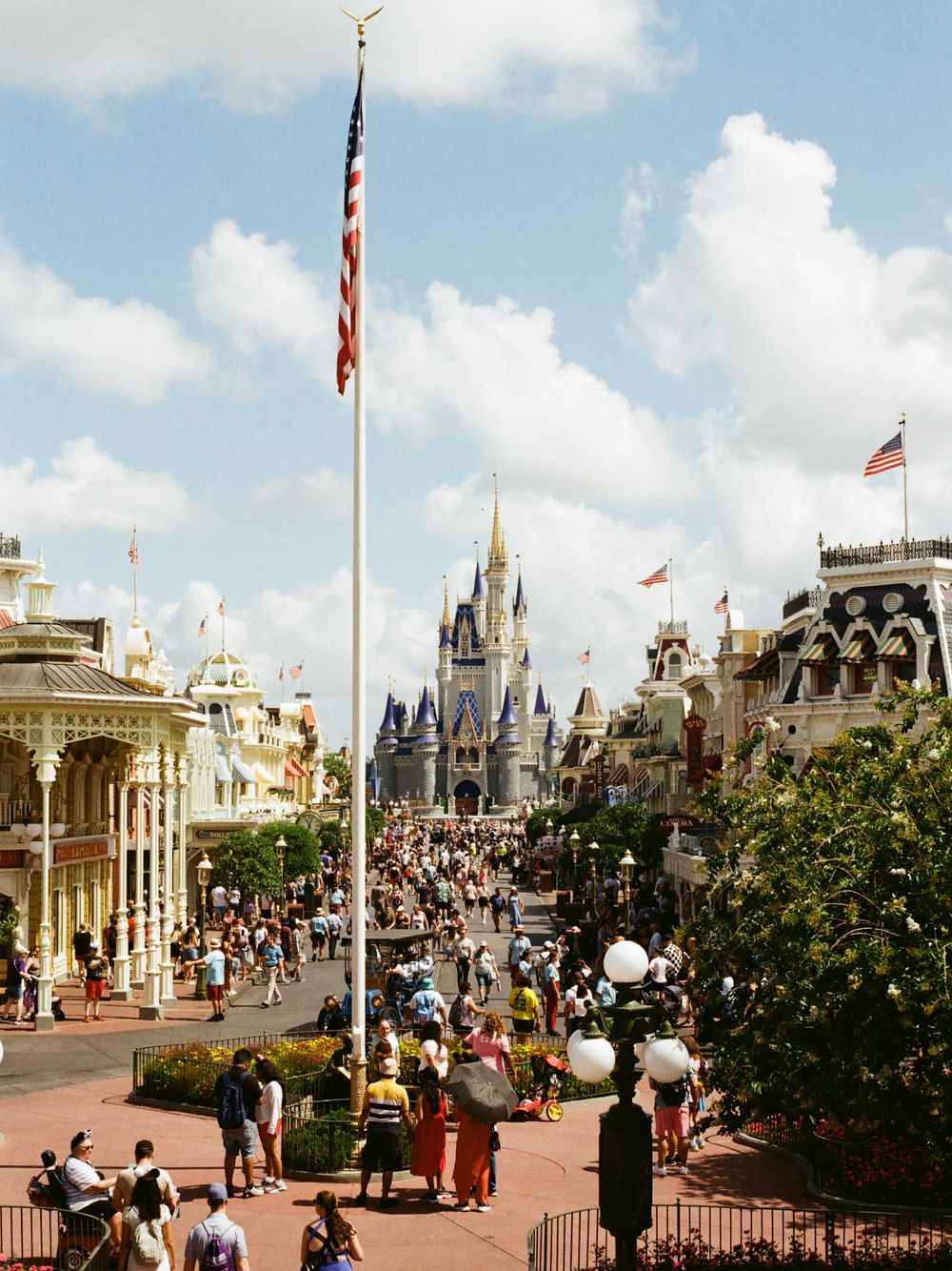 Crowded Main Street USA leads to Cinderella Castle under blue skies at Walt Disney World Magic Kingdom.