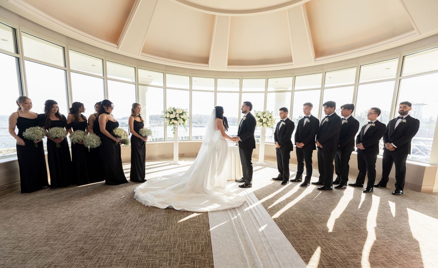 Bride and groom exchanging vows surrounded by bridesmaids and groomsmen during a waterfront wedding ceremony in New York.