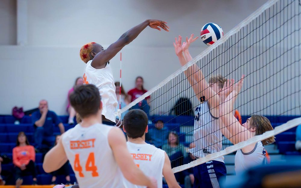 Hershey Trojan spikes as a Manheim Township player attempts to block at the net by Deanna Fox, SportsFox Photography based in Hershey PA.
