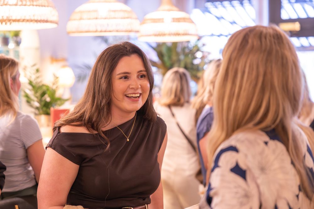 Two women networking and smiling at an indoor social event with warm lighting and decorative pendants.