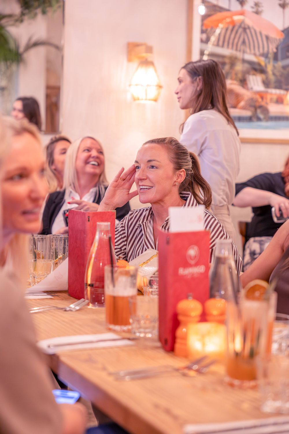 Women laughing and enjoying drinks at a warm, candlelit restaurant dining table during a social gathering.