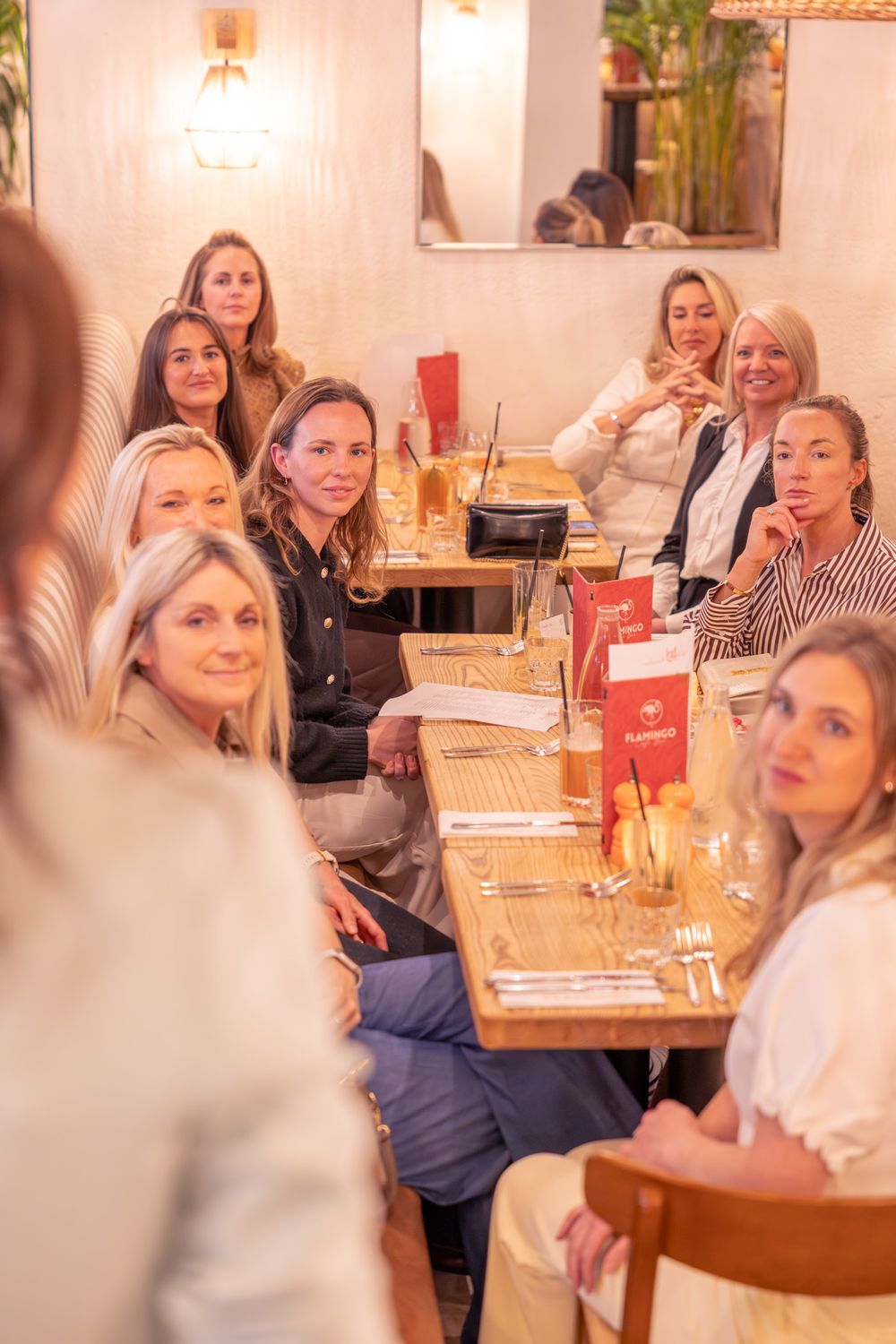 Group of women gathered around a wooden dining table in a cozy restaurant, smiling and engaged in conversation.