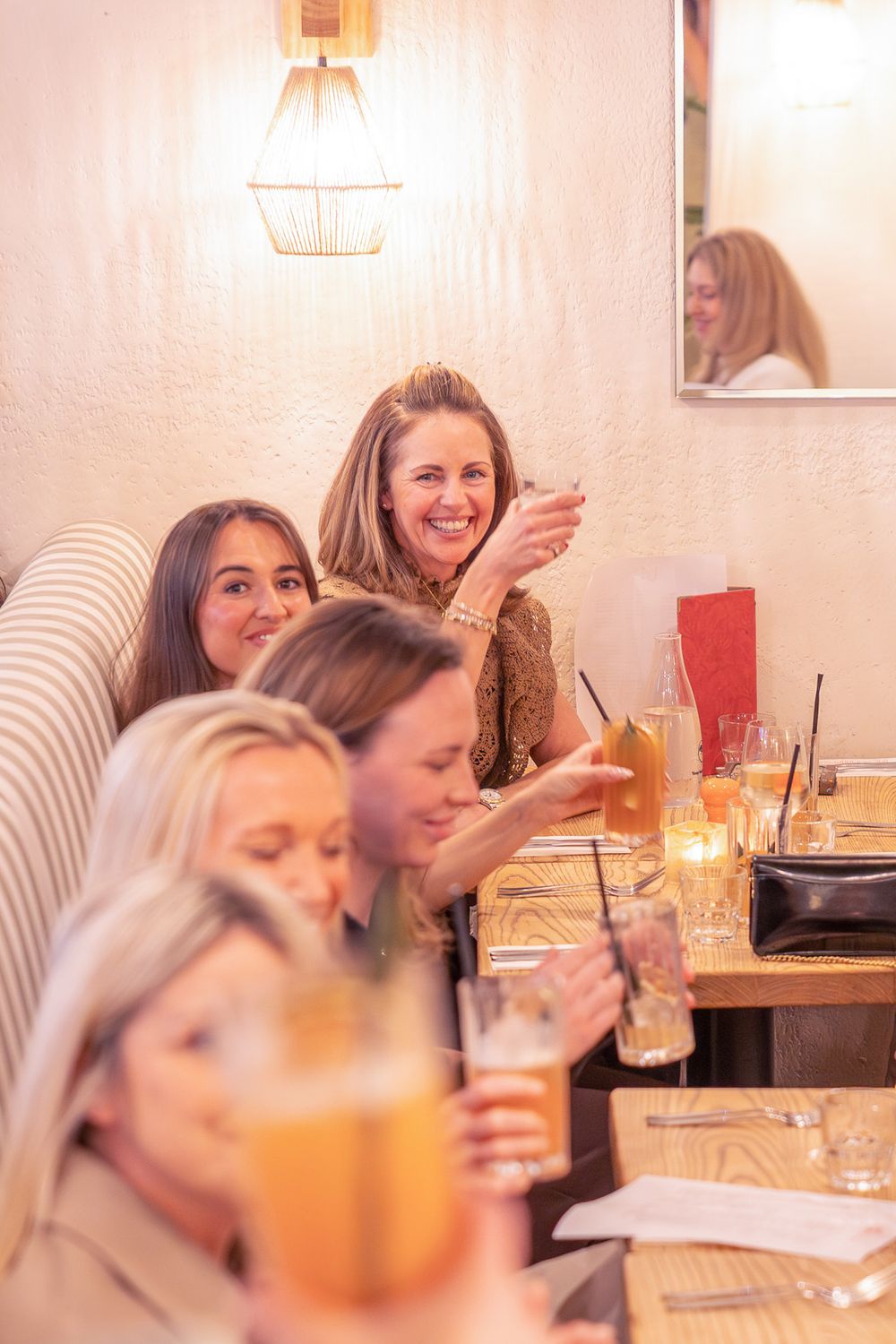 Women laughing and enjoying cocktails together at a restaurant booth, celebrating with drinks and candles on the table.