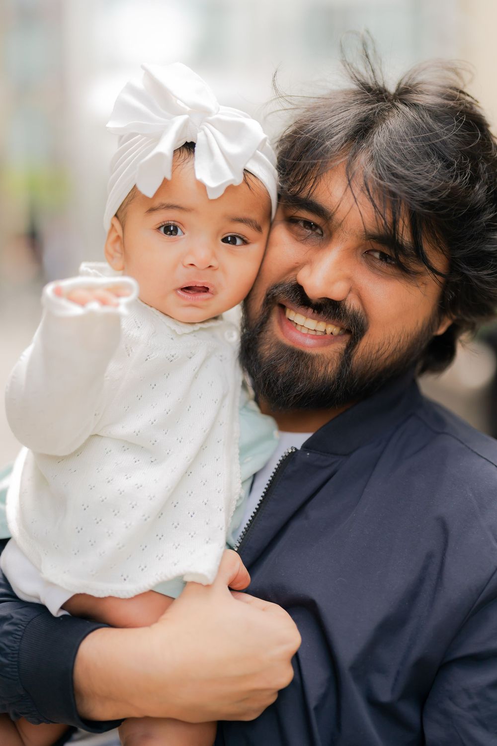 Smiling bearded man holding a cute baby girl in a white dress and bow headband.