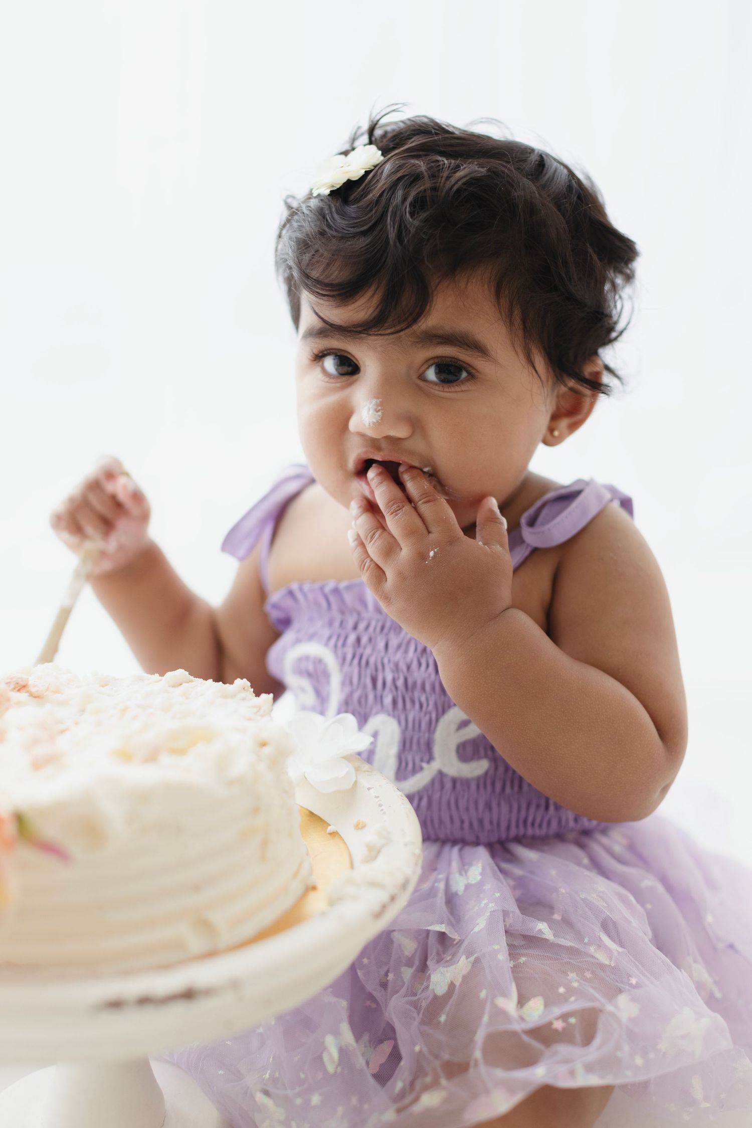 Baby girl in purple tutu dress eating birthday cake with her hands during first birthday cake smash photo session.