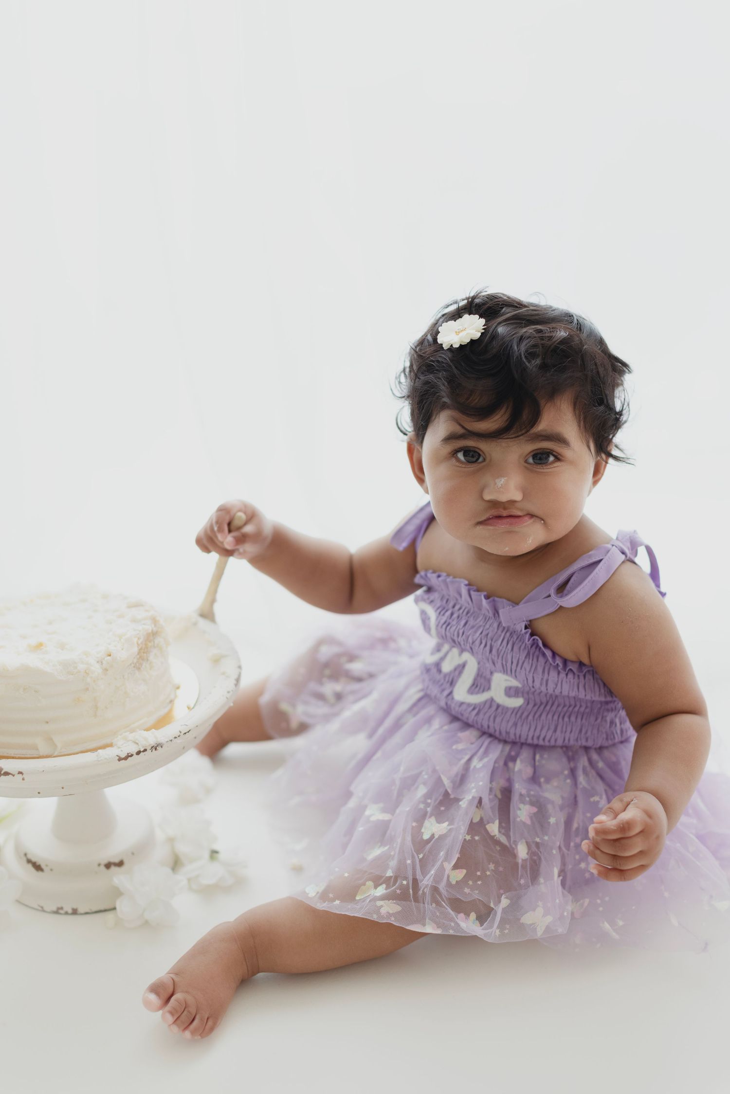 Baby girl in purple tutu dress smashing her first birthday cake on white background.
