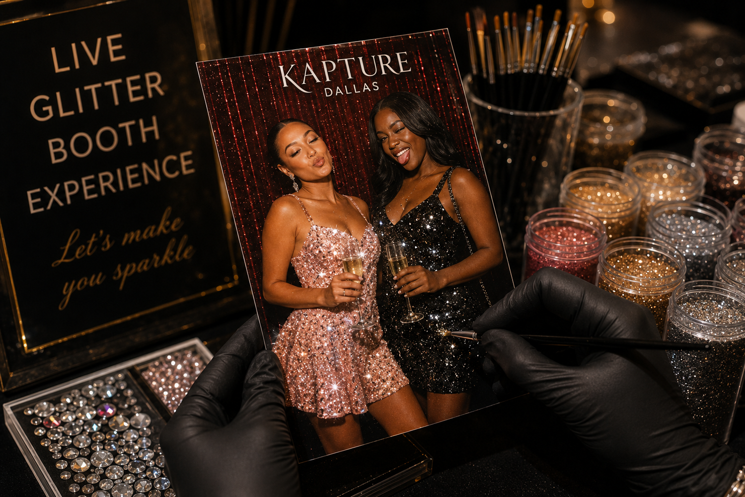Kapture Dallas glitter booth experience setup with two women in sequin dresses, glitter jars, and a Live Glitter Booth sign.