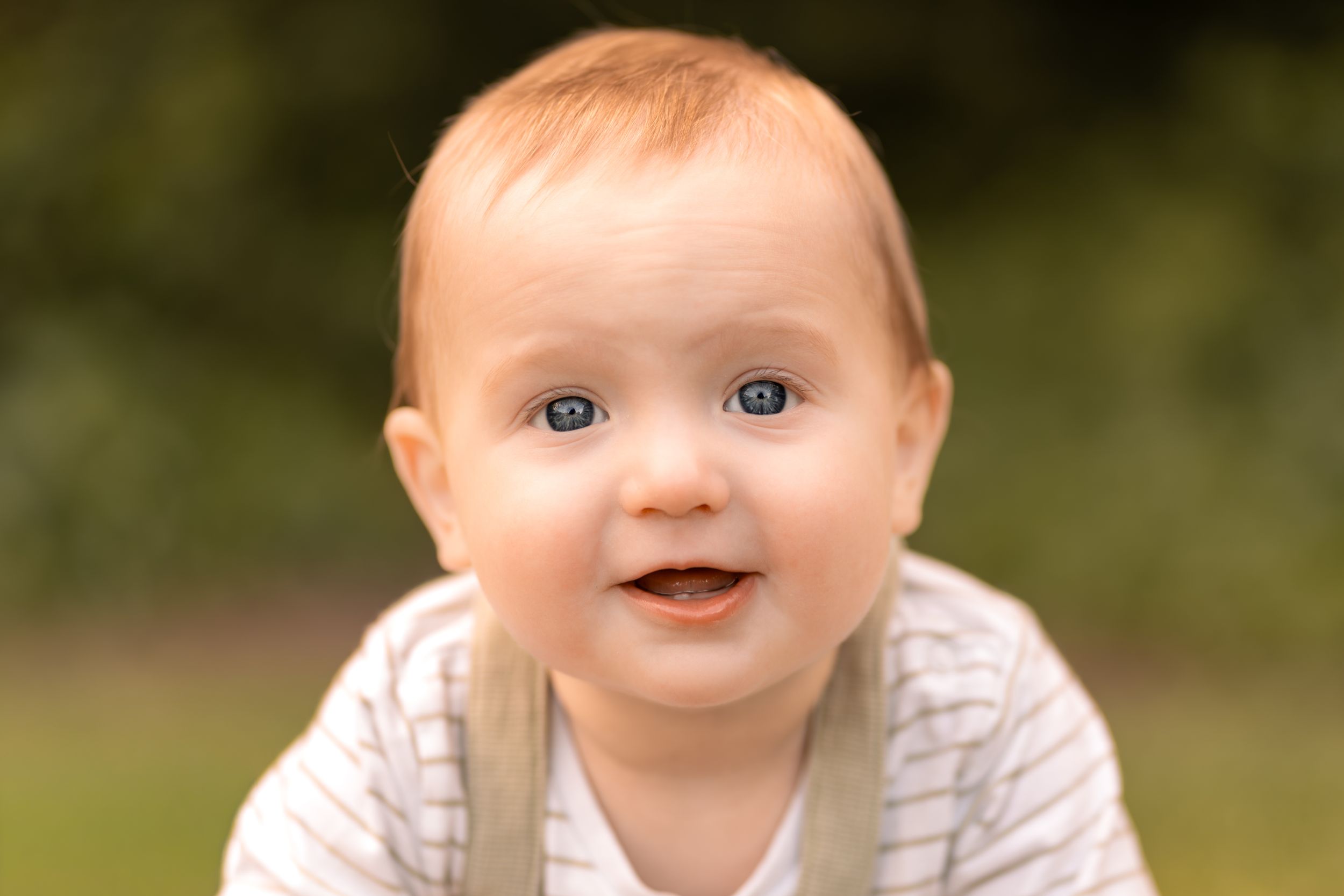 Adorable blue-eyed baby with red hair smiling outdoors during a childhood photography session in Lincolnshire.